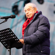 Rede von Prof. Paul Lendvai beim Fest der Freude 2025 © MKÖ/Alissar Najjar Paul Lendvai, in Winterjacke und rotem Schal, spricht beim Fest der Freude 2025, das Mikrofon und Notenpult vor sich.