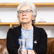 "Mauthausen-Baby" Hana Berger Moran bei der Buchpräsentation © MKÖ/Alissar Najjar Hana Berger Moran sitzt ruhig auf einem Ledersofa, vor ihr Glaskaraffen. Sie blickt leicht zur Seite.