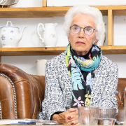 "Mauthausen-Baby" Eva Clarke bei der Buchpräsentation © MKÖ/Alissar Najjar Eva Clarke mit weißem Haar, Brille und farbigem Schal, sitzt auf einem Ledersofa, vor ihr mehrere Gläser. Sie schaut konzentriert nach vorne.